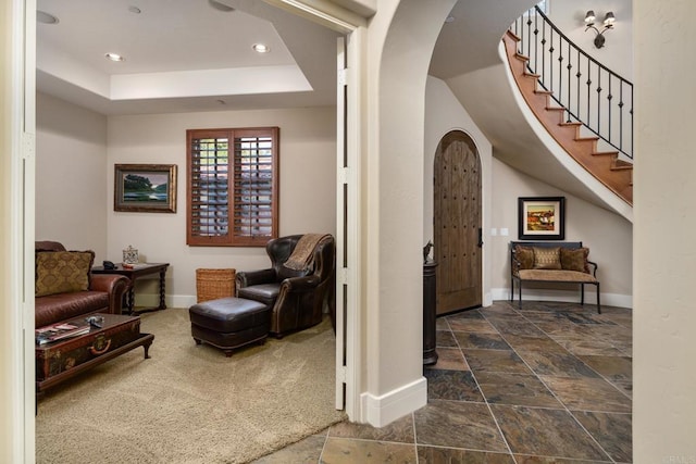 interior space with baseboards, dark carpet, a tray ceiling, stone tile floors, and arched walkways