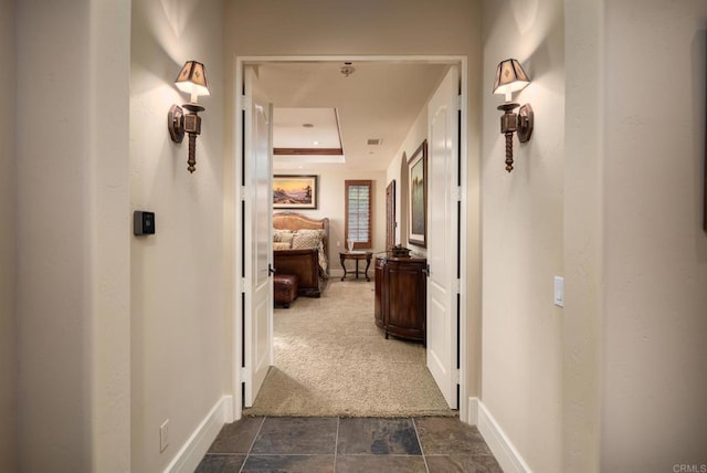 corridor featuring baseboards, dark carpet, and stone finish flooring