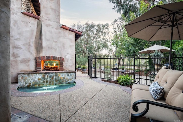 view of patio featuring a lit fireplace and fence