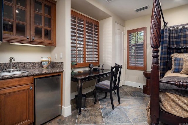 interior space featuring visible vents, a sink, dark stone counters, glass insert cabinets, and baseboards