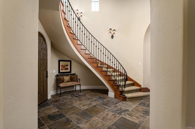 stairs featuring baseboards, arched walkways, stone tile flooring, and a towering ceiling