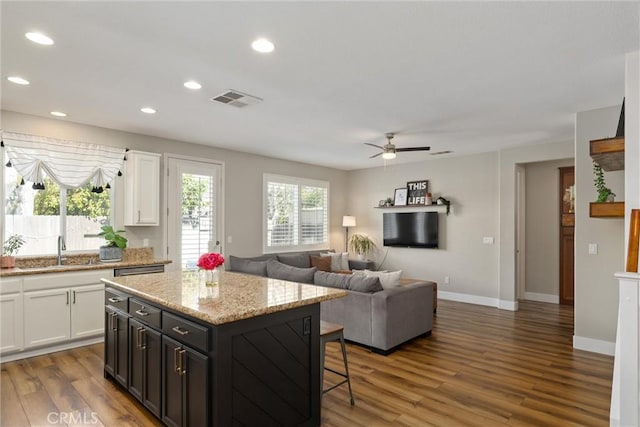 kitchen with recessed lighting, a kitchen breakfast bar, wood finished floors, white cabinets, and a sink