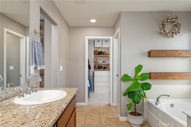 bathroom featuring vanity, baseboards, a walk in closet, a garden tub, and tile patterned floors