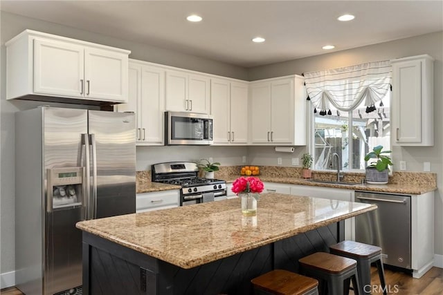 kitchen with light stone counters, white cabinetry, a sink, stainless steel appliances, and a kitchen bar