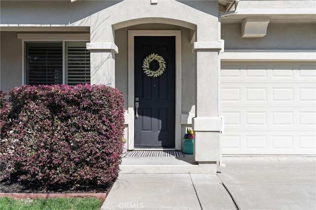 view of exterior entry with stucco siding, driveway, and an attached garage