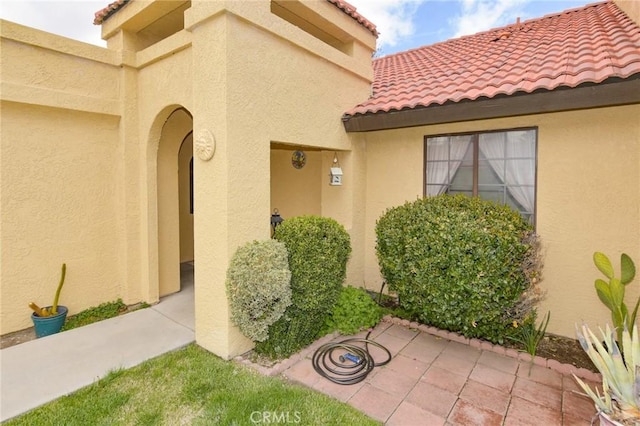 entrance to property featuring a patio area, stucco siding, and a tiled roof