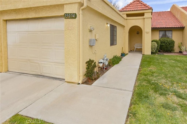 property entrance featuring a tile roof, a lawn, driveway, and stucco siding