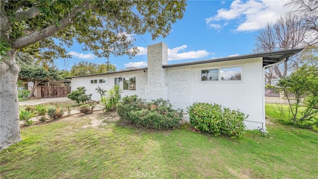 back of property featuring stucco siding, a lawn, fence, and a chimney