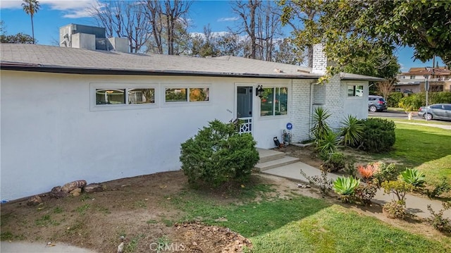 view of front of property featuring stucco siding, brick siding, a front yard, and a chimney