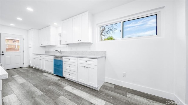 kitchen with light countertops, dishwashing machine, wood finished floors, white cabinets, and a sink