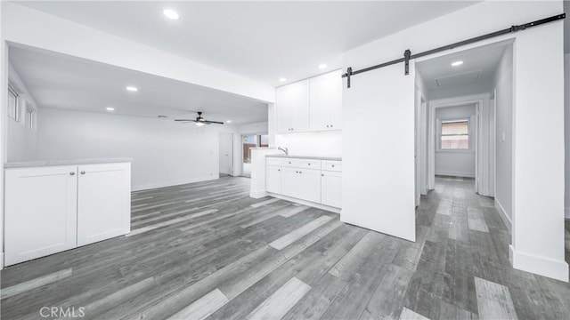 unfurnished living room with a barn door, recessed lighting, wood finished floors, and a wealth of natural light