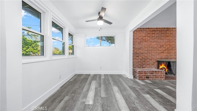 unfurnished living room with ceiling fan, a brick fireplace, baseboards, and wood finished floors