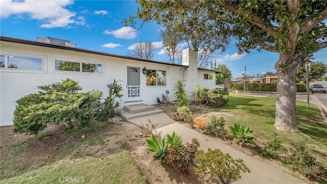 ranch-style home with stucco siding, a chimney, and a front yard