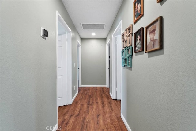 hall featuring a textured wall, baseboards, and wood finished floors