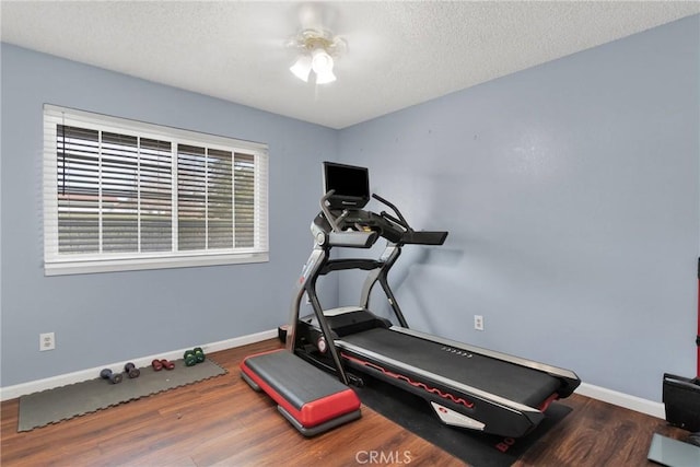 exercise area featuring wood finished floors, baseboards, and a textured ceiling