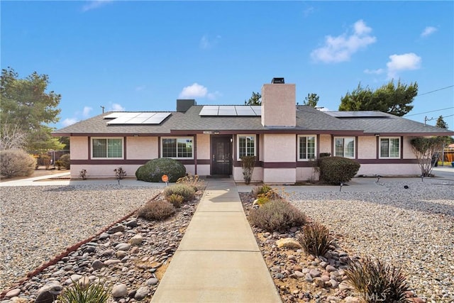 ranch-style home featuring a chimney, stucco siding, solar panels, and a shingled roof