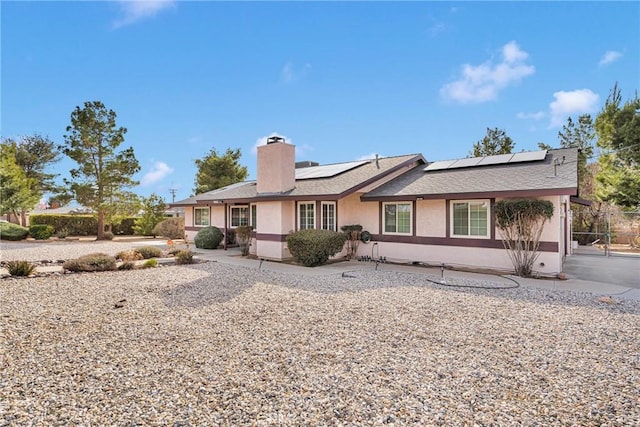 view of front of house with roof mounted solar panels, stucco siding, a chimney, and fence