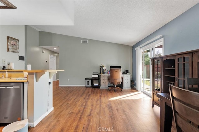 interior space with visible vents, wood finished floors, baseboards, dishwasher, and vaulted ceiling