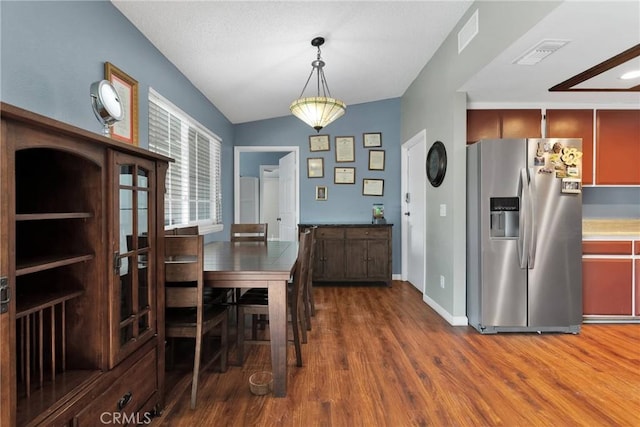 dining room with lofted ceiling, wood finished floors, visible vents, and baseboards