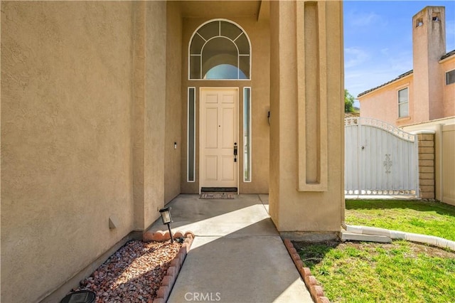 view of exterior entry featuring a gate and stucco siding