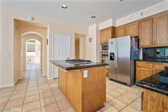 kitchen with arched walkways, appliances with stainless steel finishes, light tile patterned flooring, and a center island