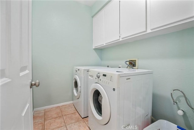 clothes washing area with washer and dryer, light tile patterned flooring, cabinet space, and baseboards