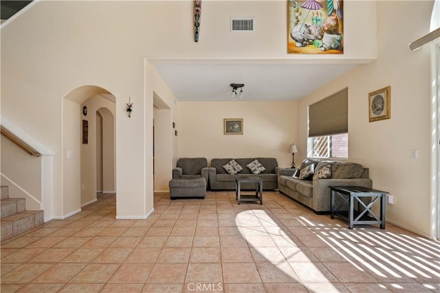 living room with stairs, light tile patterned flooring, arched walkways, and visible vents