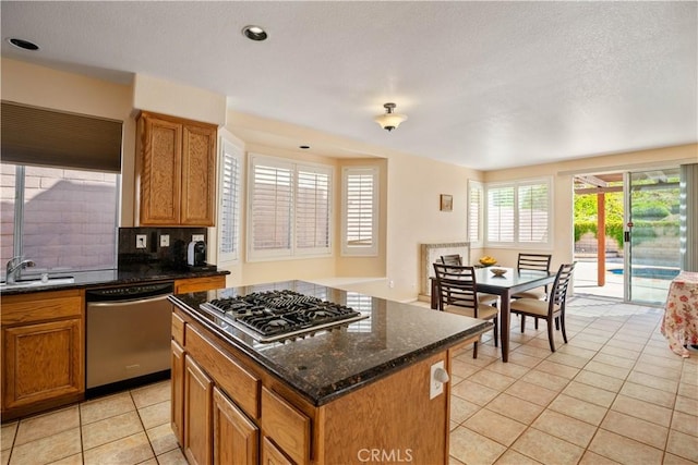 kitchen with a center island, light tile patterned floors, appliances with stainless steel finishes, brown cabinetry, and a sink