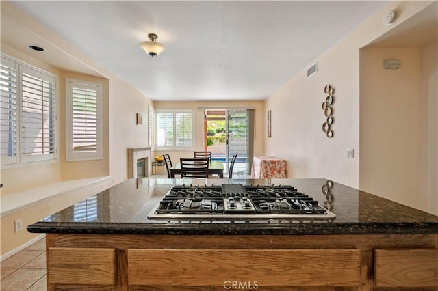 kitchen with visible vents, a center island, stainless steel gas cooktop, dark stone counters, and light tile patterned floors