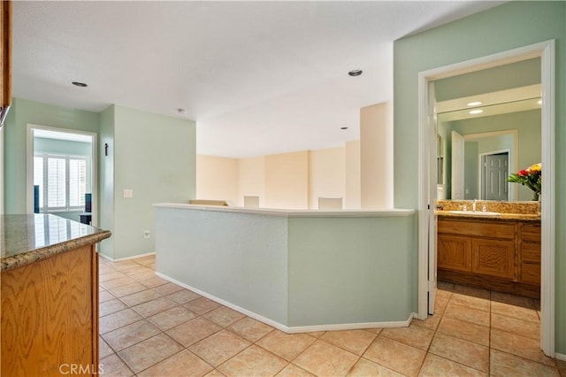 kitchen featuring light tile patterned floors, baseboards, a sink, light countertops, and brown cabinets