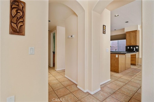 hallway featuring light tile patterned floors, baseboards, arched walkways, and recessed lighting