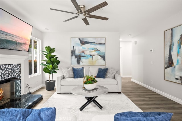 living area featuring baseboards, wood finished floors, a ceiling fan, and a tiled fireplace