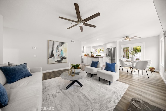 living area featuring plenty of natural light, baseboards, light wood finished floors, and ceiling fan