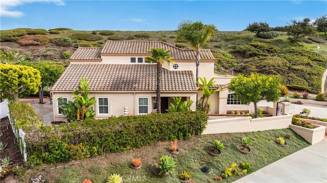 mediterranean / spanish house featuring stucco siding, a tile roof, a vegetable garden, and fence