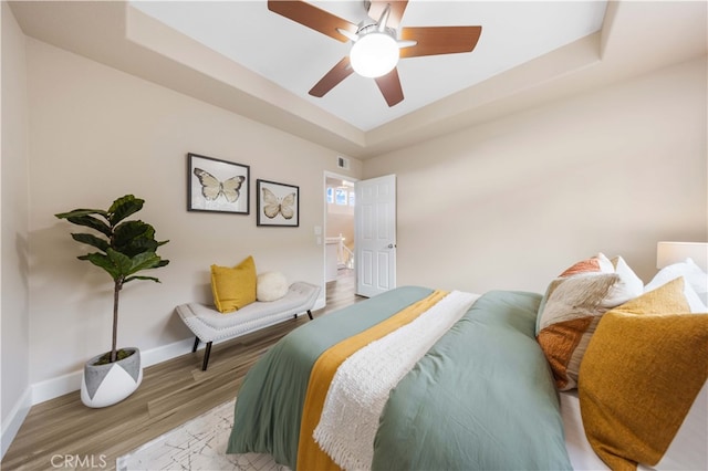 bedroom with ceiling fan, baseboards, a raised ceiling, and wood finished floors