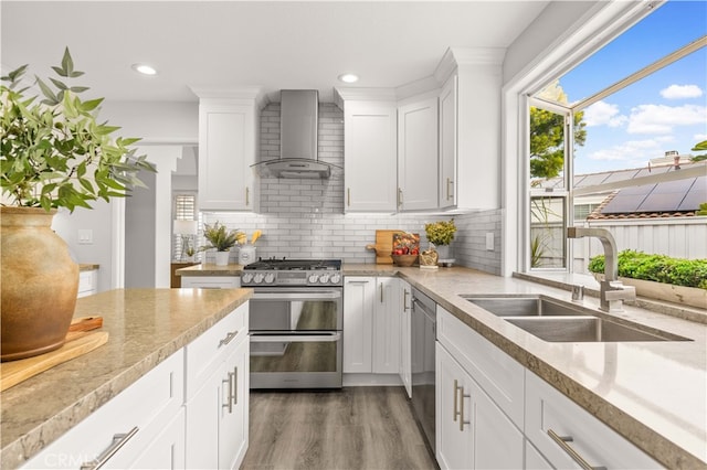 kitchen featuring a sink, backsplash, wood finished floors, stainless steel appliances, and wall chimney range hood