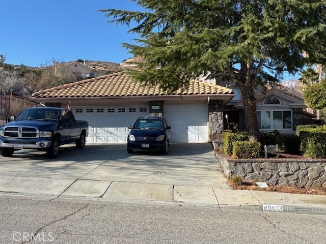 ranch-style home with a tile roof, concrete driveway, stone siding, and an attached garage