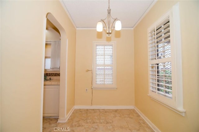 unfurnished dining area with baseboards, arched walkways, a notable chandelier, and ornamental molding