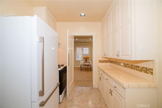 kitchen featuring tasteful backsplash, black gas stove, freestanding refrigerator, white cabinets, and tile counters