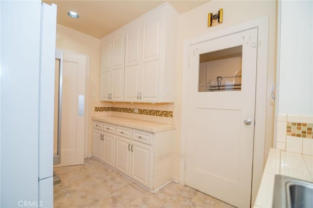 interior space with tasteful backsplash, tile countertops, and white cabinets