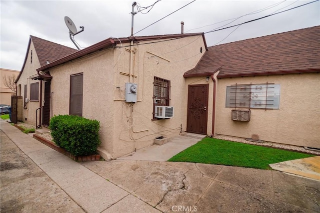 view of front of property featuring stucco siding, roof with shingles, and cooling unit