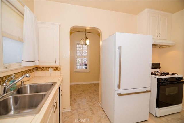 kitchen with under cabinet range hood, gas range, freestanding refrigerator, arched walkways, and a sink