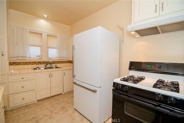 kitchen featuring under cabinet range hood, tile countertops, range with gas stovetop, freestanding refrigerator, and a sink