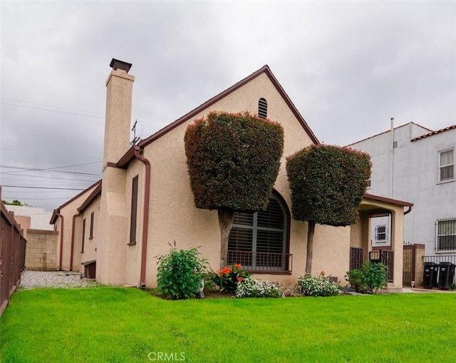 back of property with a chimney, fence, a lawn, and stucco siding