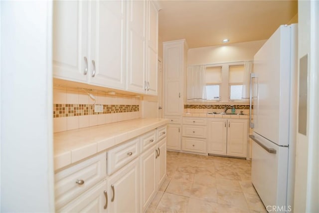 kitchen with backsplash, tile countertops, recessed lighting, freestanding refrigerator, and white cabinets