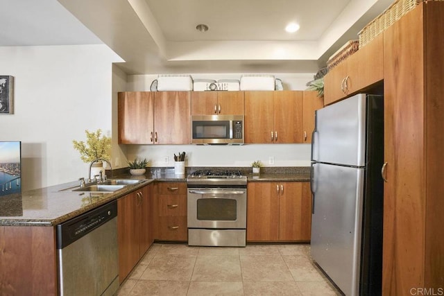 kitchen with a peninsula, light tile patterned flooring, a sink, stainless steel appliances, and brown cabinets