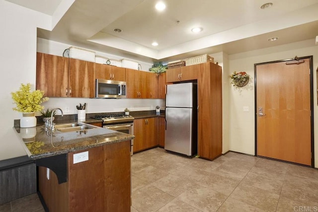 kitchen featuring brown cabinetry, a tray ceiling, a peninsula, a sink, and stainless steel appliances