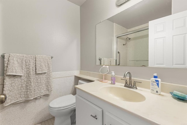 full bathroom with a wainscoted wall, toilet, tile walls, a shower stall, and vanity