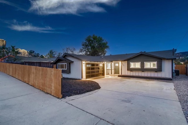 view of front facade with board and batten siding, concrete driveway, an attached garage, and fence