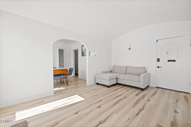 living area with vaulted ceiling, wood finished floors, arched walkways, and baseboards